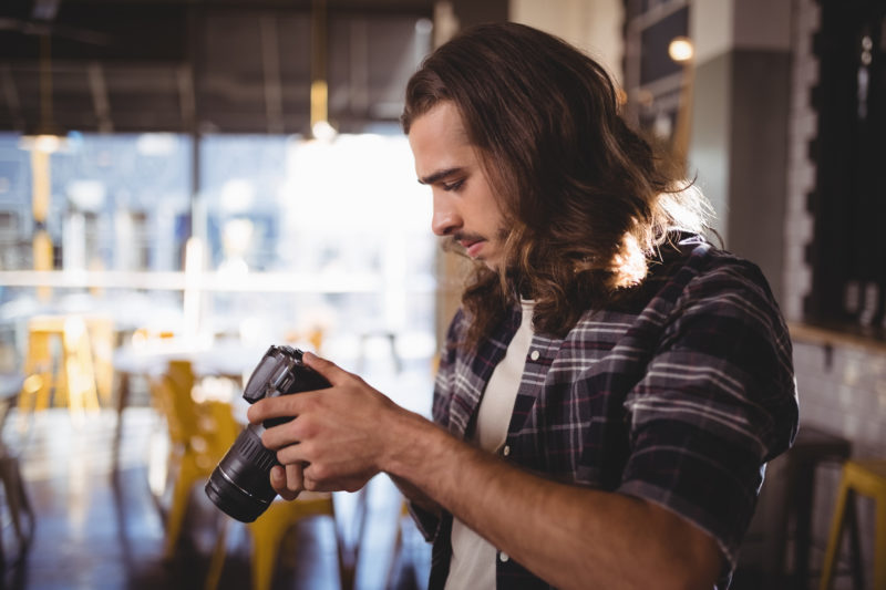 Zijaanzicht van jonge mannelijke fotograaf die DSLR-camera houdt